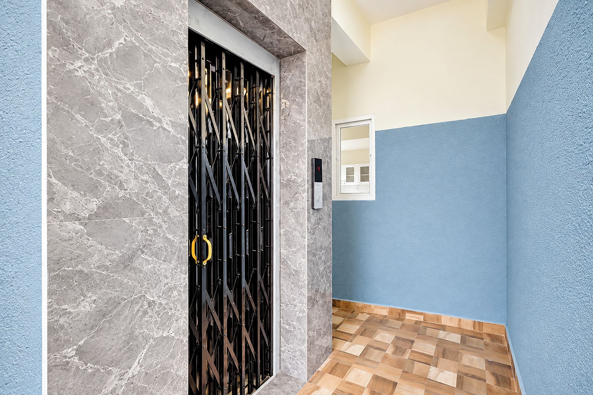 Um corredor com parede de mármore, porta de metal preta com puxador dourado e piso de madeira.