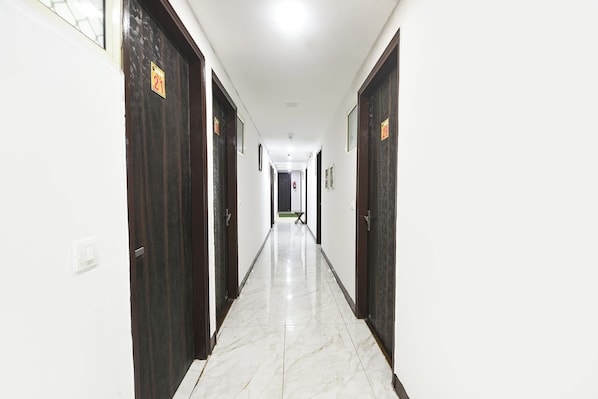 Pasillo de hotel con puertas numeradas, piso de baldosas e iluminación en el techo.