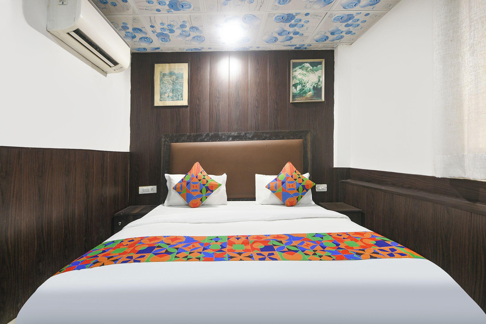 Habitación de hotel con cama, dos almohadas, cabecero y techo con motivos florales.
