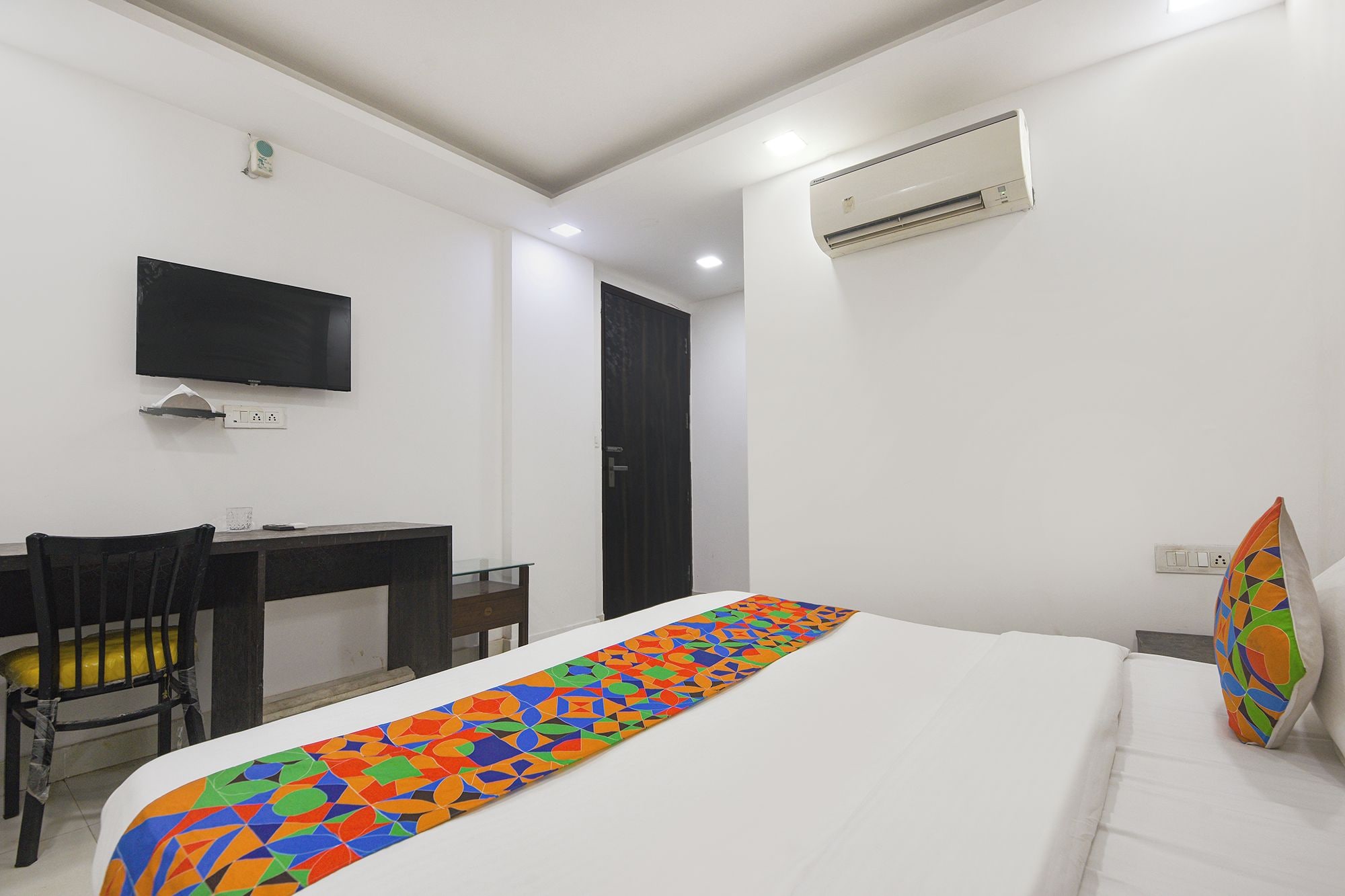 Habitación de hotel con cama, escritorio, silla, televisor y aire acondicionado.