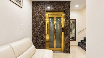 A hotel lobby with a marble wall, a white leather sofa, and a glass elevator.