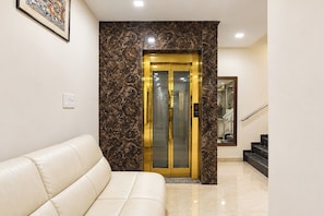 Un hall de hotel con pared de mármol, sofá de cuero blanco y ascensor de vidrio.