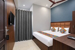 Una habitación de hotel con una cama, un escritorio, un televisor y un ventilador de techo.