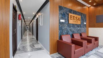 A hotel reception area with a marble floor, wooden paneling, a reception desk, and a seating area with red chairs.
