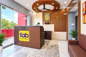 Zona de recepción de un hotel, con mostrador de recepción que dice 'fab hotels', un ventilador de techo y un cartel de recepción.
