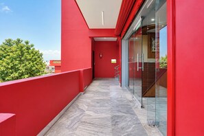 Pasillo exterior rojo con puerta de vidrio que da a una escalera.