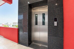 Un ascensor moderno con pantalla digital que muestra el número 2, rodeado por una pared roja y un suelo negro pulido.