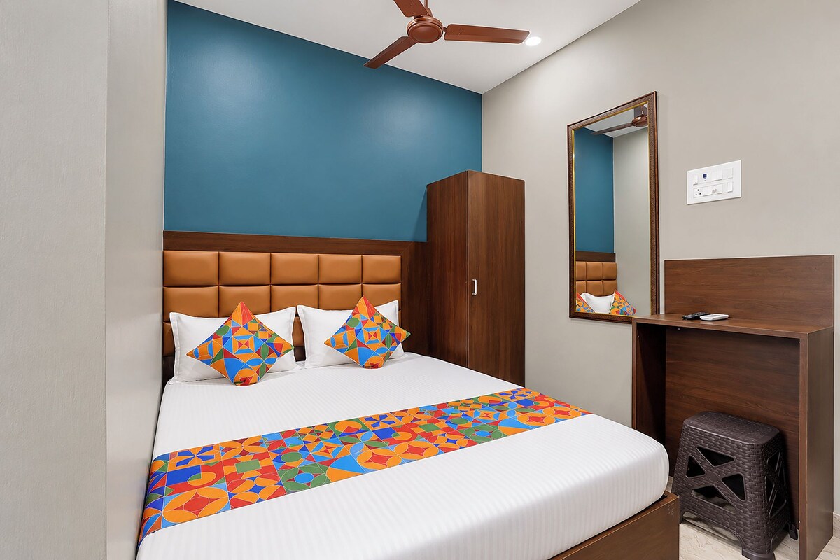 Una habitación de hotel con cama, armario, espejo, ventilador de techo y un taburete pequeño.