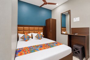 Una habitación de hotel con cama, armario, escritorio, espejo y ventilador de techo.