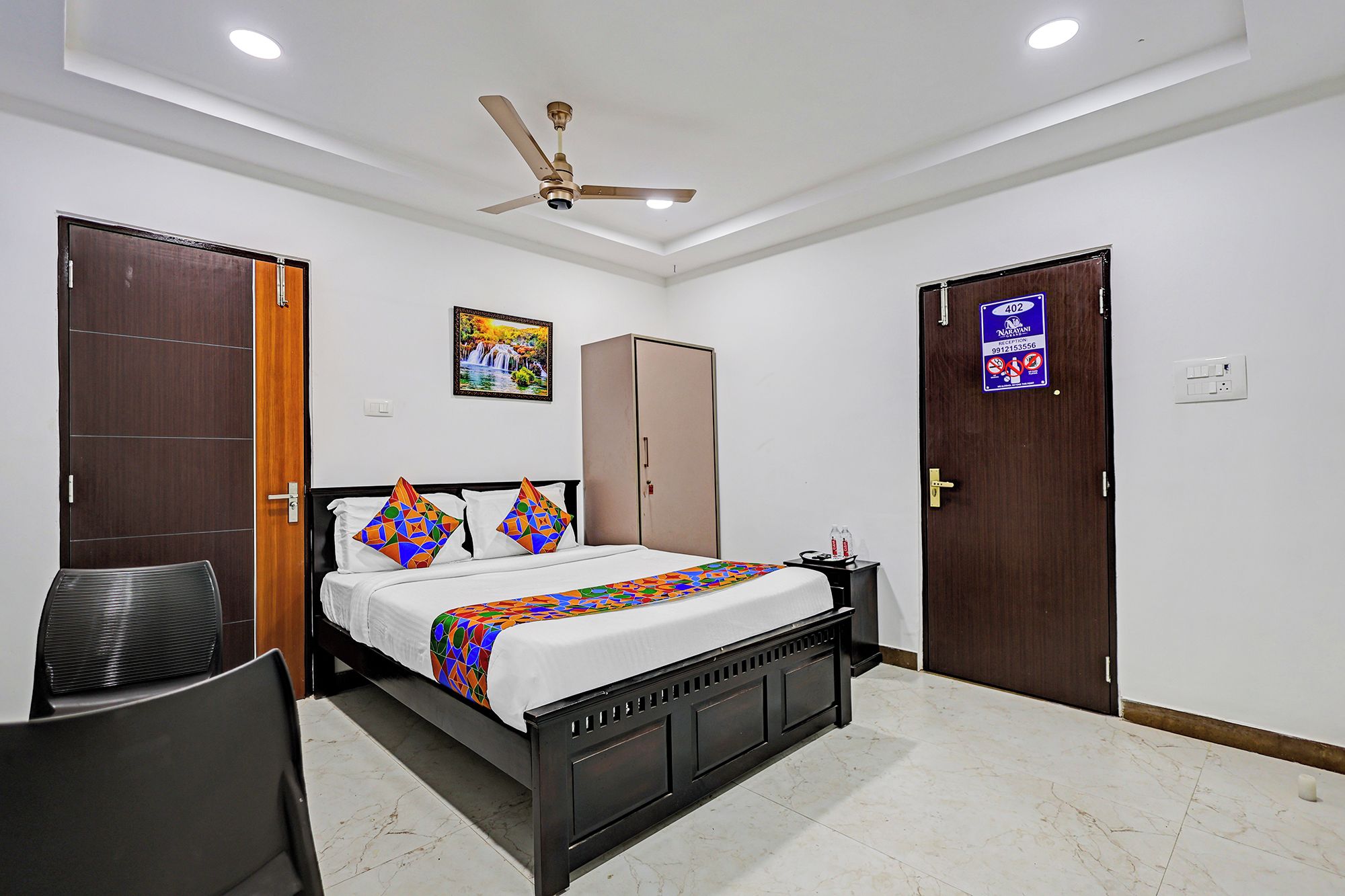 A hotel room with a bed, wardrobe, desk, chair, and a ceiling fan.