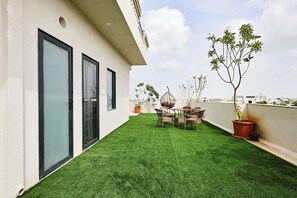 Una terrazza sul tetto con erba sintetica, un tavolo con sedie, piante in vaso e vista sulla città.