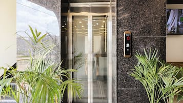 An elevator with a digital display, glass doors, and potted plants beside it.