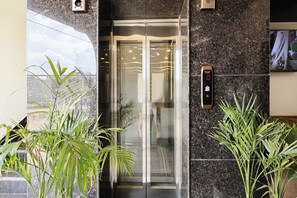 Un ascensor con pantalla digital, puertas de vidrio y plantas en macetas a su lado.
