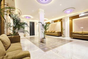 Una hall d'hotel moderna con pavimento in marmo, due divani, piante in vaso e illuminazione a incasso.