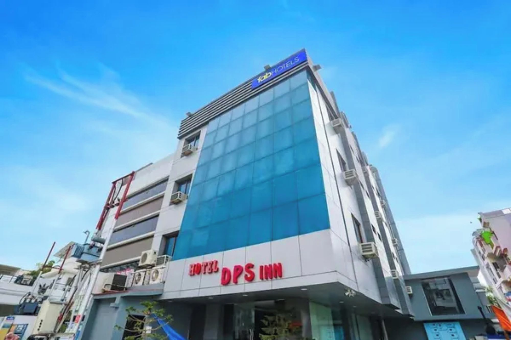 A modern hotel building with a prominent sign for 'HOTEL DPS INN' and a blue glass facade.