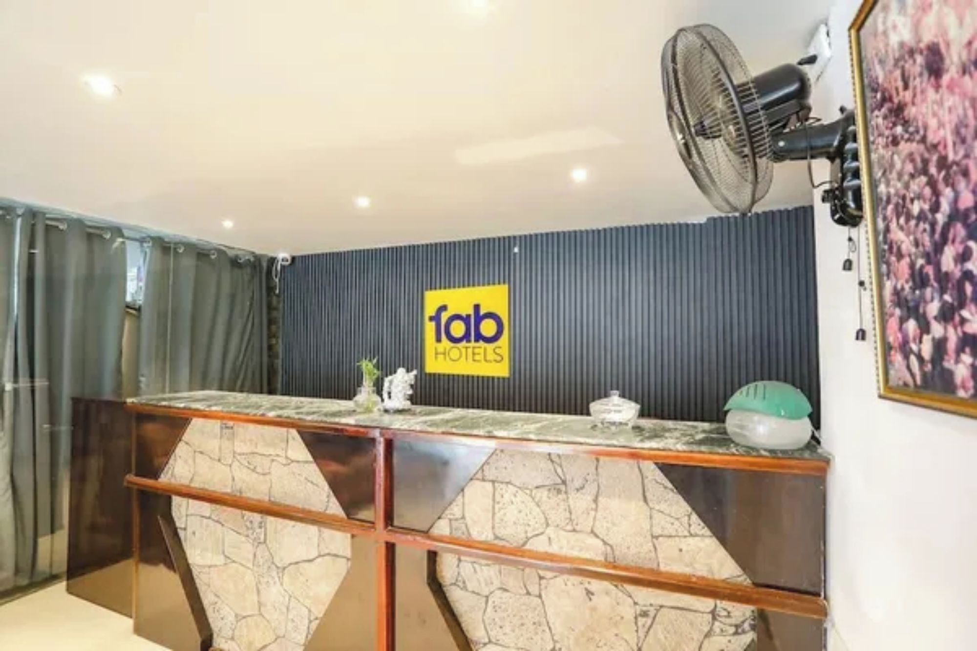 A hotel reception area with a counter, a fan, and a logo on the wall.