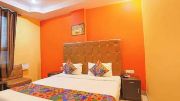 A hotel room with a large bed, orange walls, and a tufted headboard.