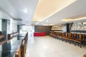 Una amplia sala de conferencias con una larga mesa y filas de sillas, un telón rojo de fondo y una pared de acento de piedra.