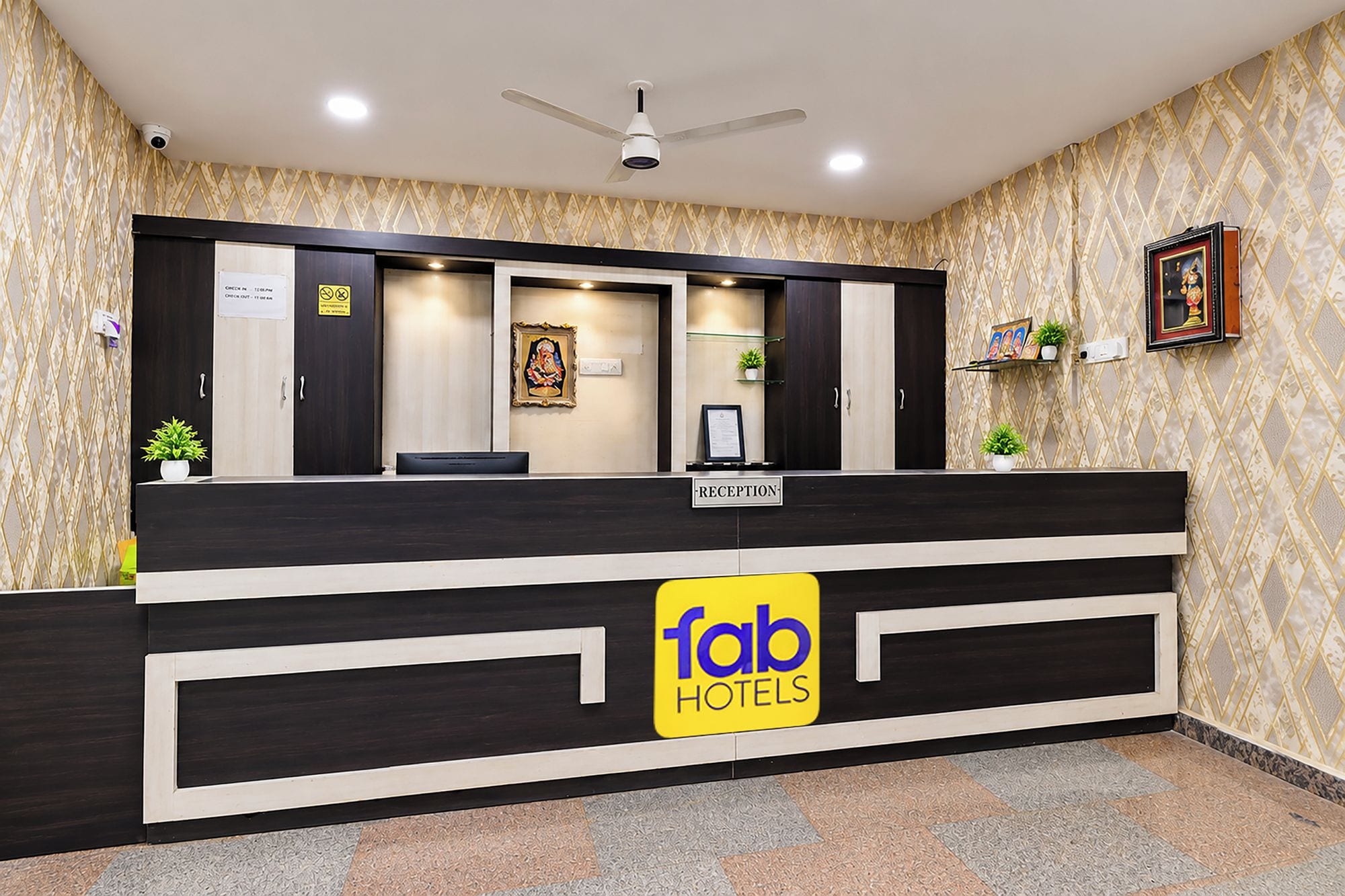 Un mostrador de recepción con un letrero de 'fab hotels', un ventilador de techo y una pared estampada.