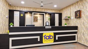 Un mostrador de recepción con un letrero de 'fab hotels', un ventilador de techo y una pared estampada.