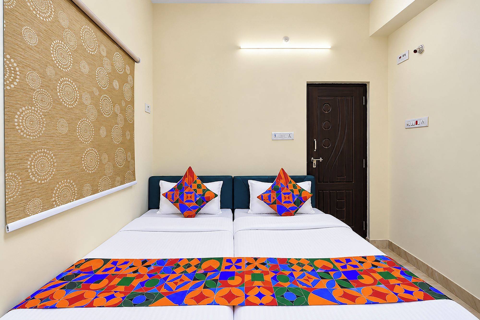 A hotel room with a bed, two pillows, a patterned curtain, a door, and a light fixture.