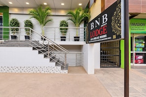 Entrada de un hotel con escaleras, plantas en macetas y un letrero que indica Habitaciones con y sin aire acondicionado BNB Lodge.