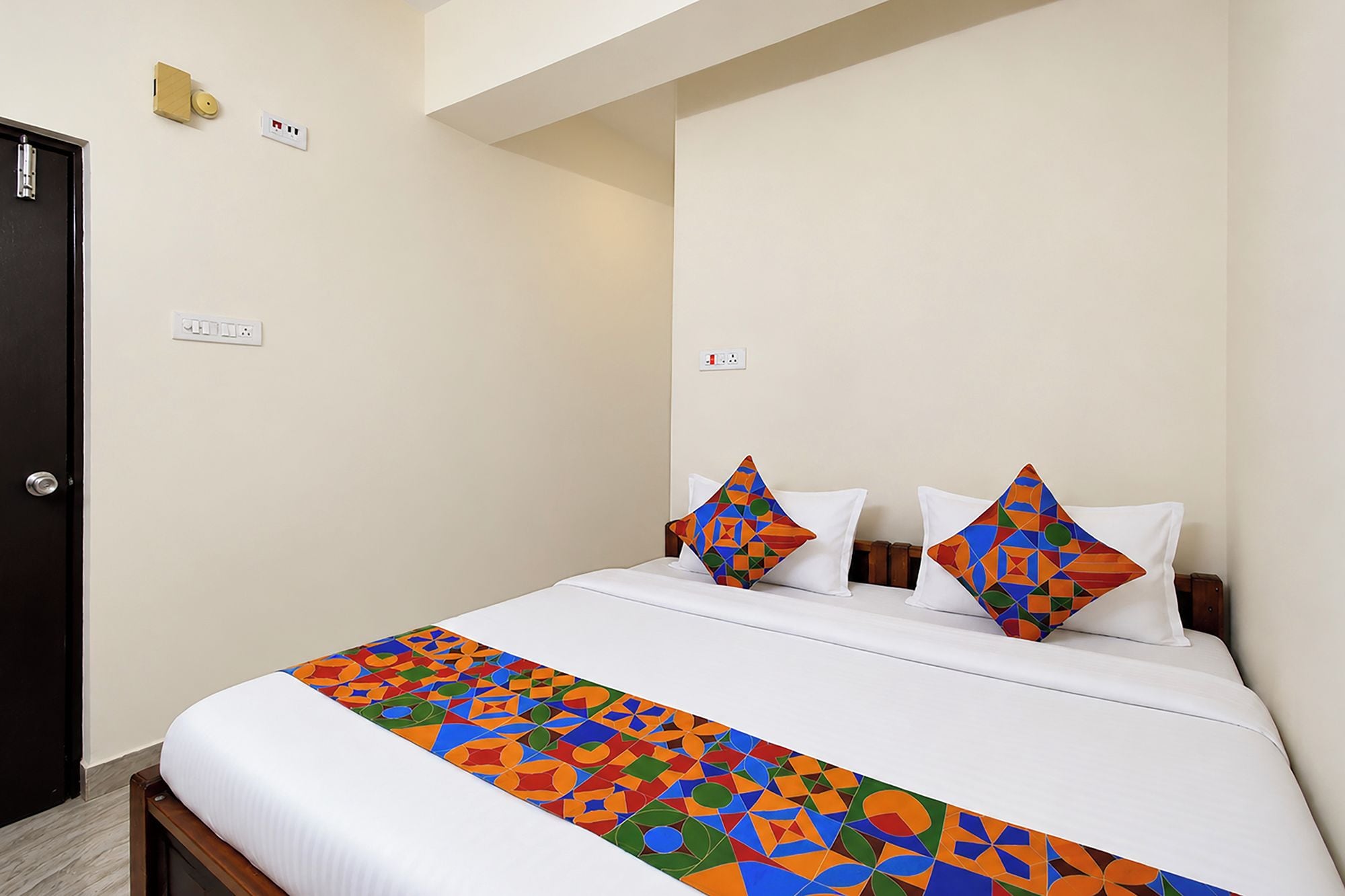 Habitación de hotel con cama, dos almohadas, mesita de noche y toma de corriente.
