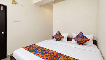 Habitación de hotel con cama, dos almohadas, mesita de noche y toma de corriente.
