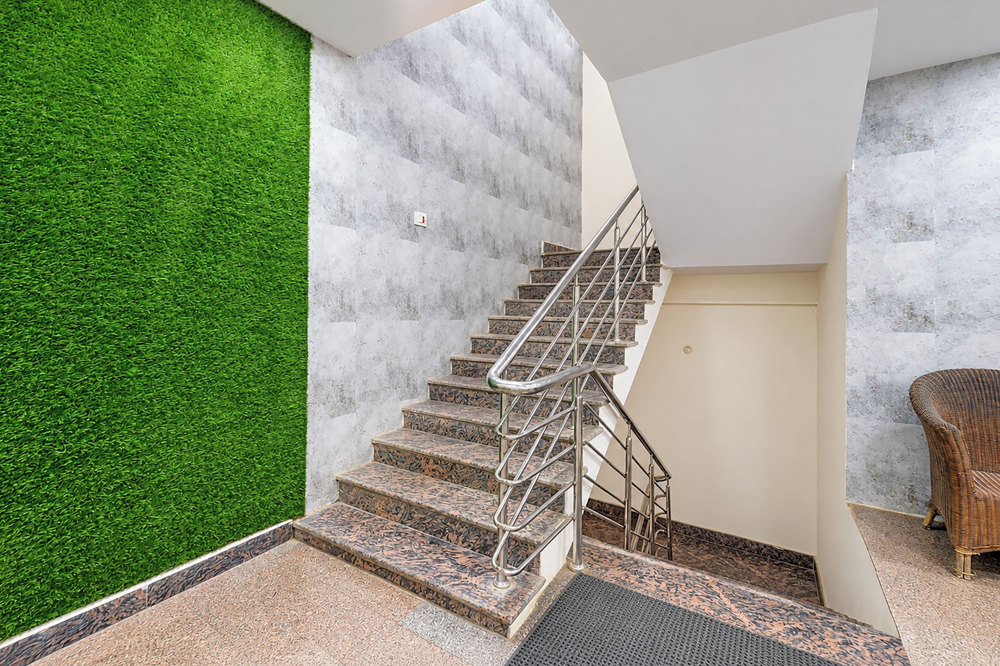 Una escalera con barandilla de metal, pared verde y una silla de mimbre.