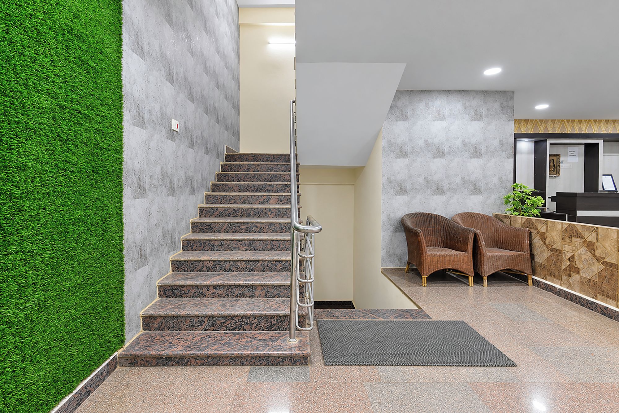Una escalera con barandillas metálicas que conduce a una zona de recepción con un mostrador y dos sillas de mimbre.