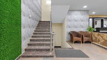 Una escalera con barandillas metálicas que conduce a una zona de recepción con un mostrador y dos sillas de mimbre.