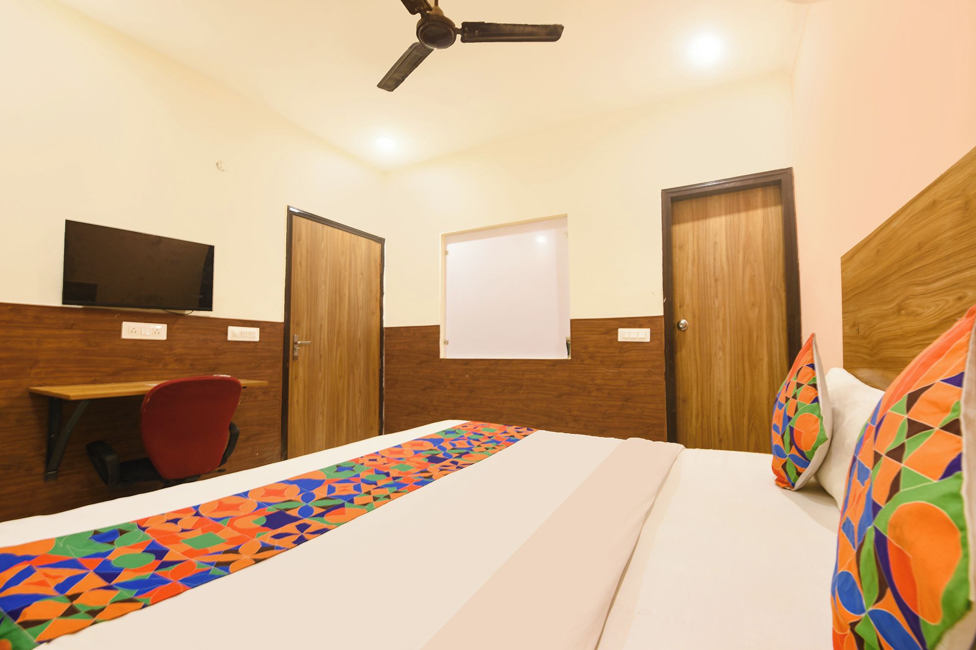 Una habitación de hotel con cama, escritorio, silla, televisor y ventilador de techo.