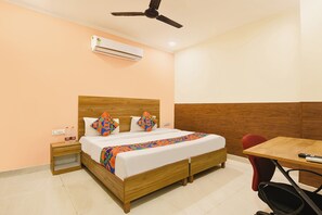 A hotel room with a wooden bed, a desk, a chair, an air conditioner, and a ceiling fan. - FabHotel Royal Inn Ii (New Delhi)