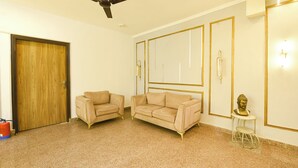 Una habitación con ventilador de techo, dos sofás, una mesita, una estatua de Buda y una puerta de madera.