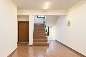 A hallway with a wooden door, a staircase with a metal railing, and a light fixture on the ceiling. - FabHotel Royal Inn Ii (New Delhi)