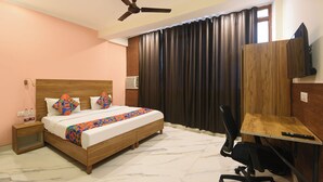 Una habitación de hotel con una cama, un escritorio, una silla, un ventilador de techo y una ventana con cortinas.