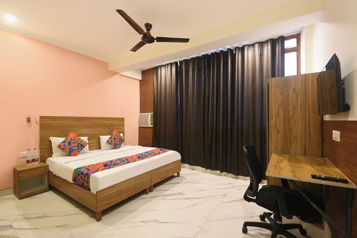 Una habitación de hotel con una cama, un escritorio, una silla, un ventilador de techo y una ventana con cortinas.