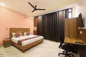Una habitación de hotel con una cama, un escritorio, una silla, un ventilador de techo y una ventana con cortinas.
