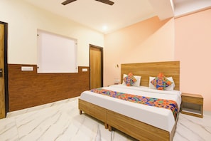 A hotel room with a bed, wooden headboard, a nightstand, and a wall-mounted TV. - FabHotel Royal Inn Ii (New Delhi)