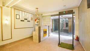 Zona de recepción de un hotel con un mostrador, certificados enmarcados, un reloj y una estación de control de seguridad.