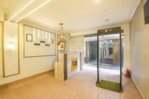 Zona de recepción de un hotel con un mostrador, certificados enmarcados, un reloj y una estación de control de seguridad.