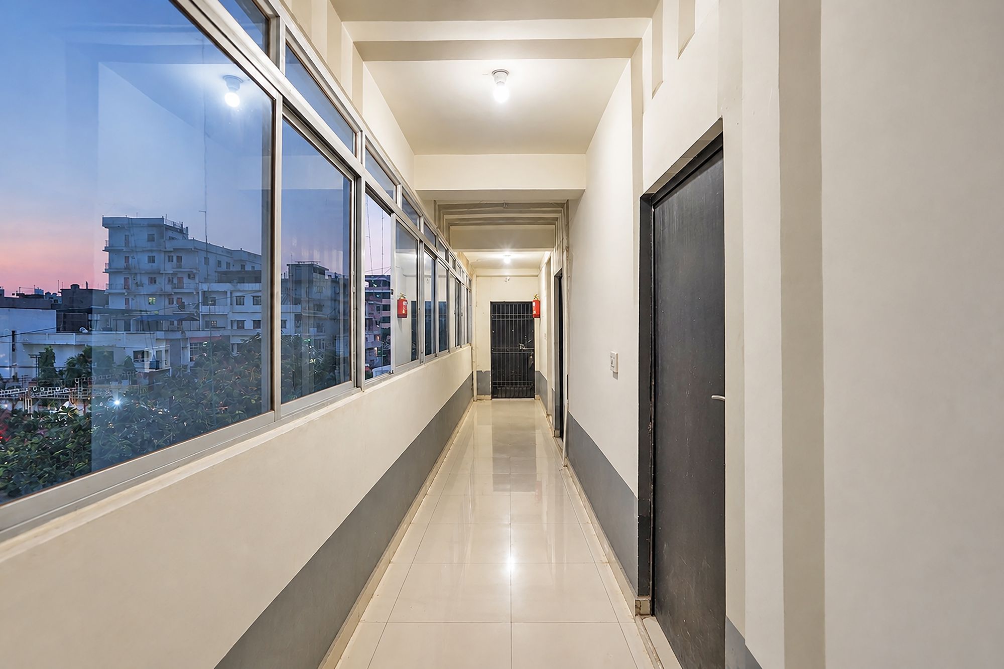 Un pasillo con ventanas amplias, una puerta y un extintor.