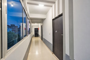 Un pasillo con vistas a edificios exteriores, una puerta con un número y un detector de incendios.