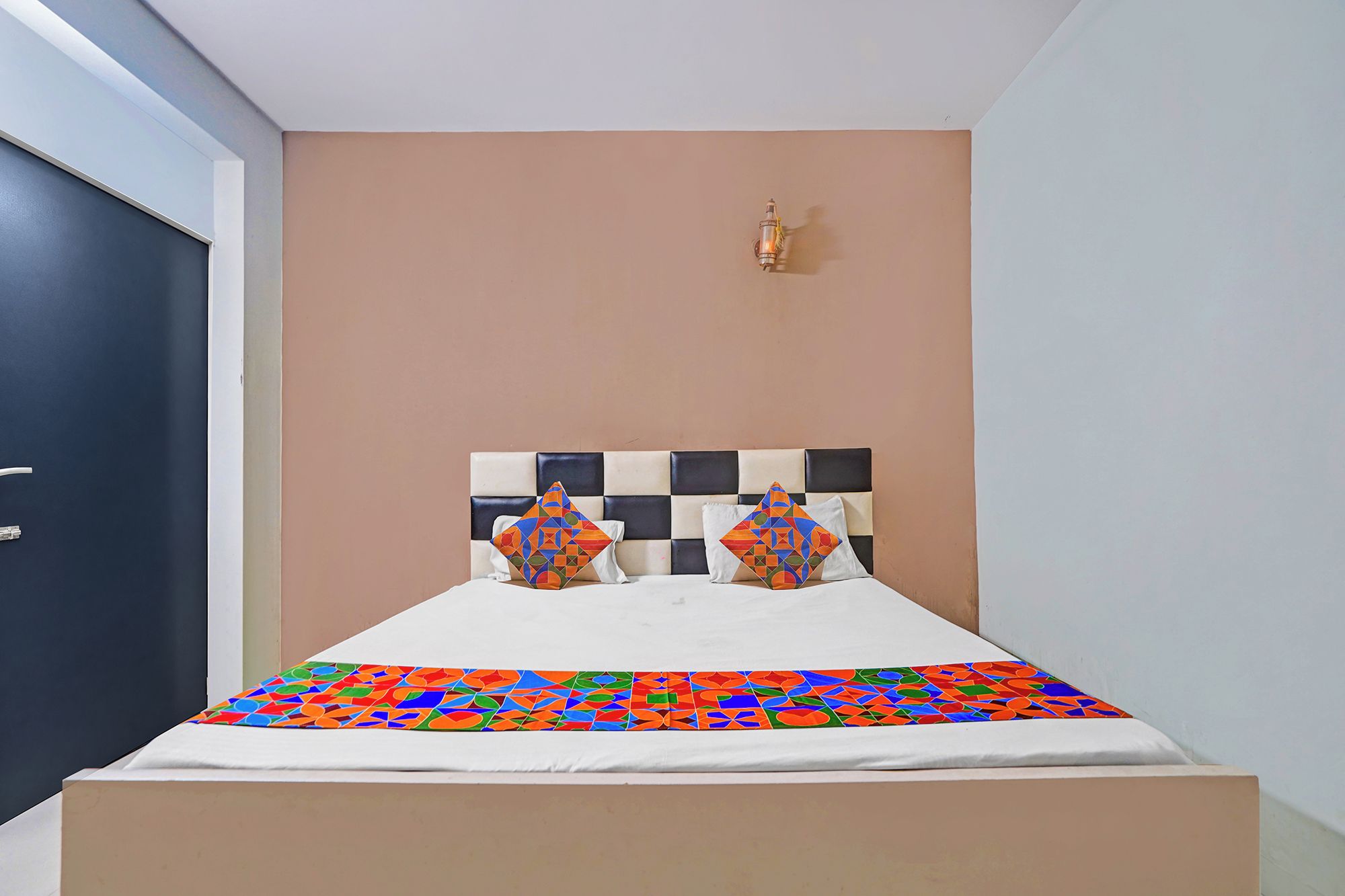 Una cama con cabecera a cuadros, dos almohadas con diseños geométricos y una colcha colorida.