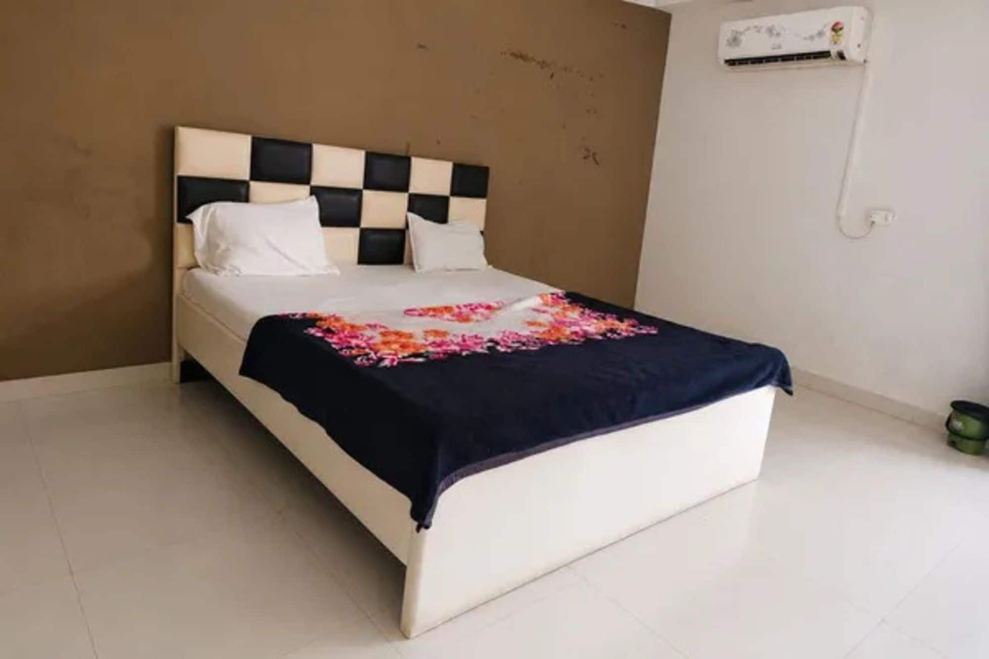 Una cama con cabecera de cuadros, una colcha estampada con motivos florales y un colchón blanco.
