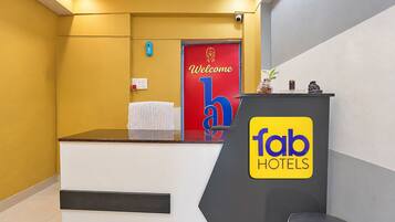 Una recepción con un cartel de 'fab hotels', una puerta roja con un letrero de bienvenida y una lámpara azul fijada a la pared.