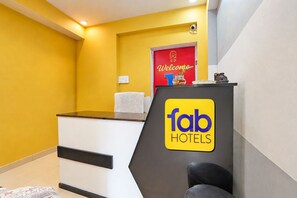 A reception desk with a 'fab hotels' sign, a red door with a welcome sign, and a small plant on top. - FabHotel Ab (Patna)