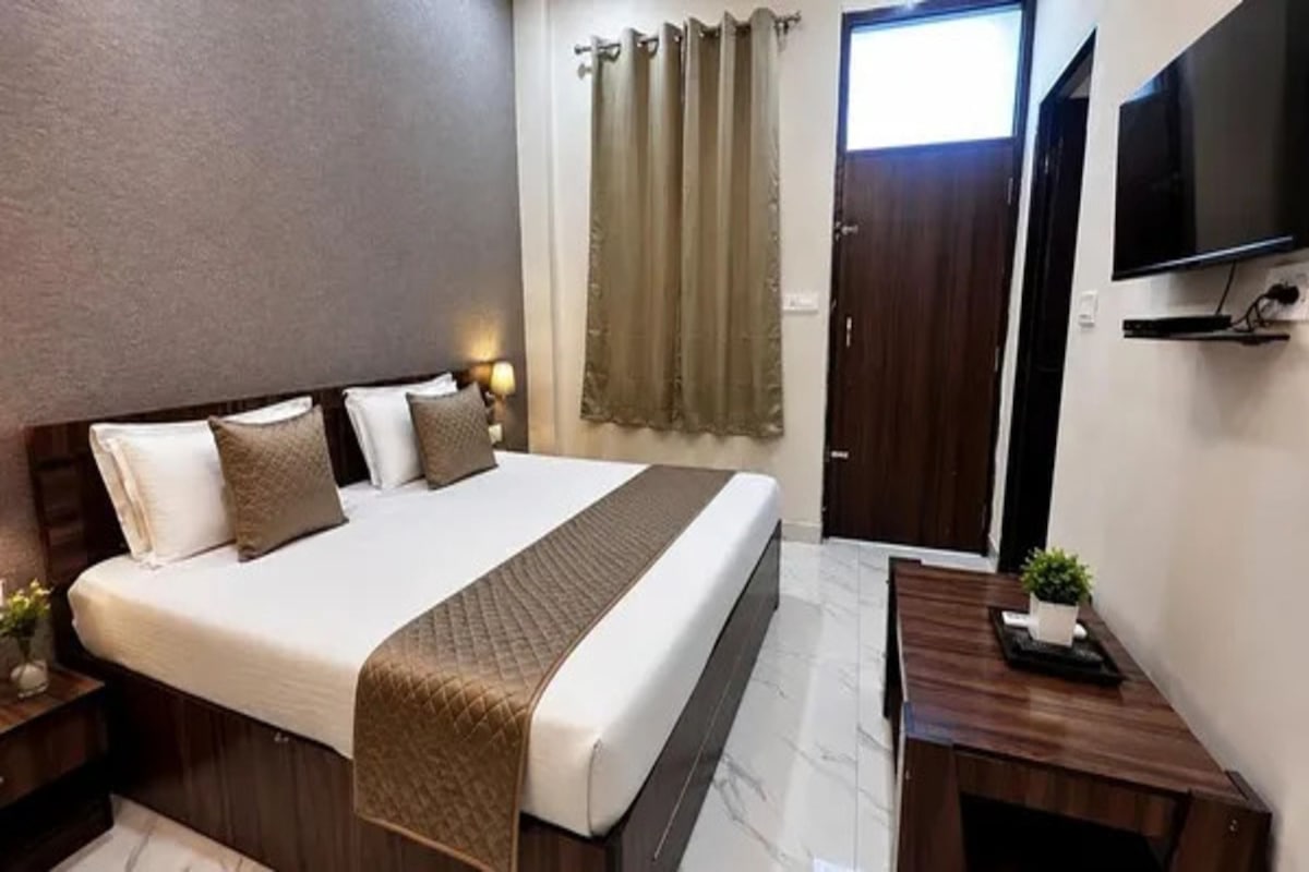 A hotel room with a bed, bedside tables, a desk, a television, and a window with curtains.