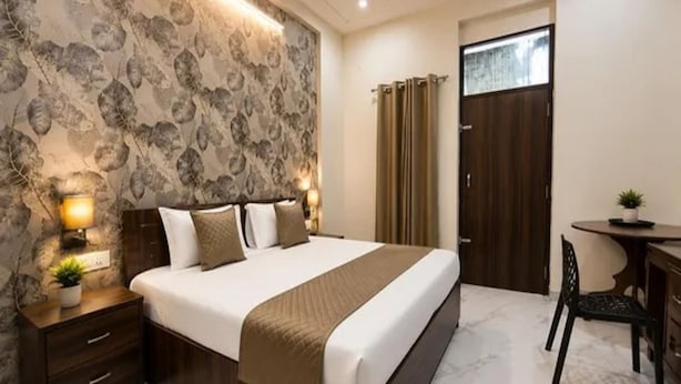 A hotel room with a large bed, bedside lamps, a desk with a chair, and a door with curtains. - Fabhotel Raadhe (Khatoo)