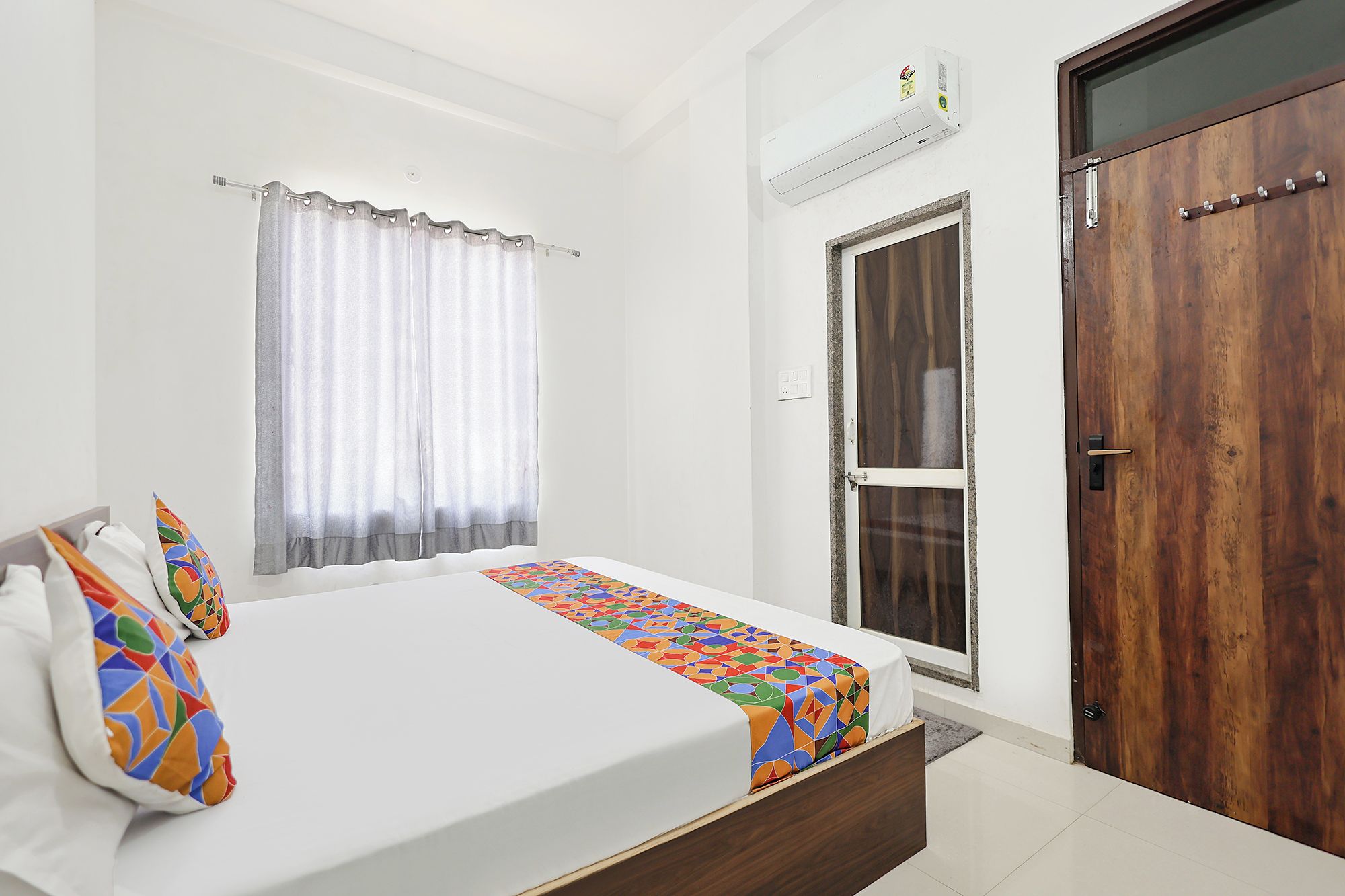 Un dormitorio con cama, ventana con cortinas, una puerta y un equipo de aire acondicionado.